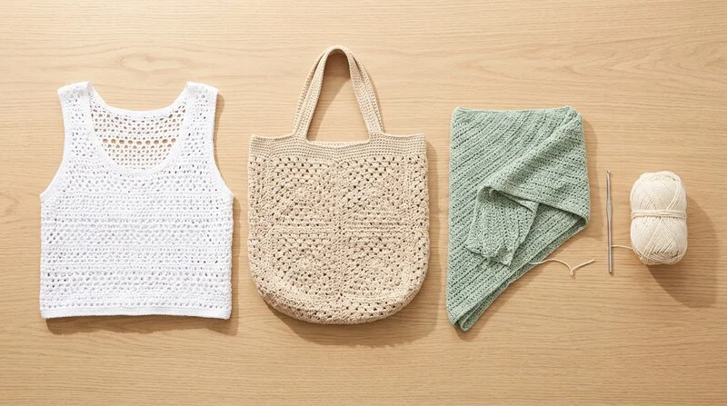 Plusieurs modèles crochet été en coton léger posés sur une table en bois : top ajouré, sac granny, châle triangulaire