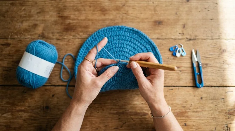 Mains travaillant un ouvrage au crochet avec de la laine bleue et un crochet en bois