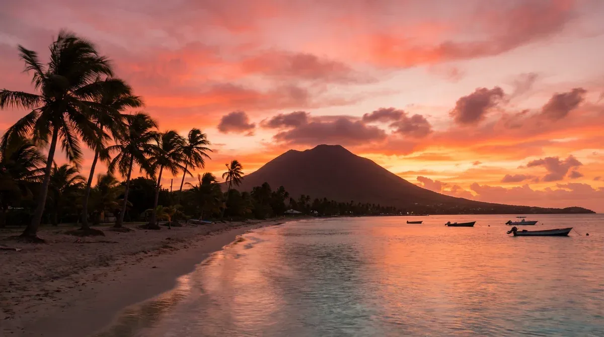 Nevis island coastline at golden hour sunset showing calm Caribbean Sea waters reflecting orange and pink sky colors, silhouette of Nevis Peak, palm t