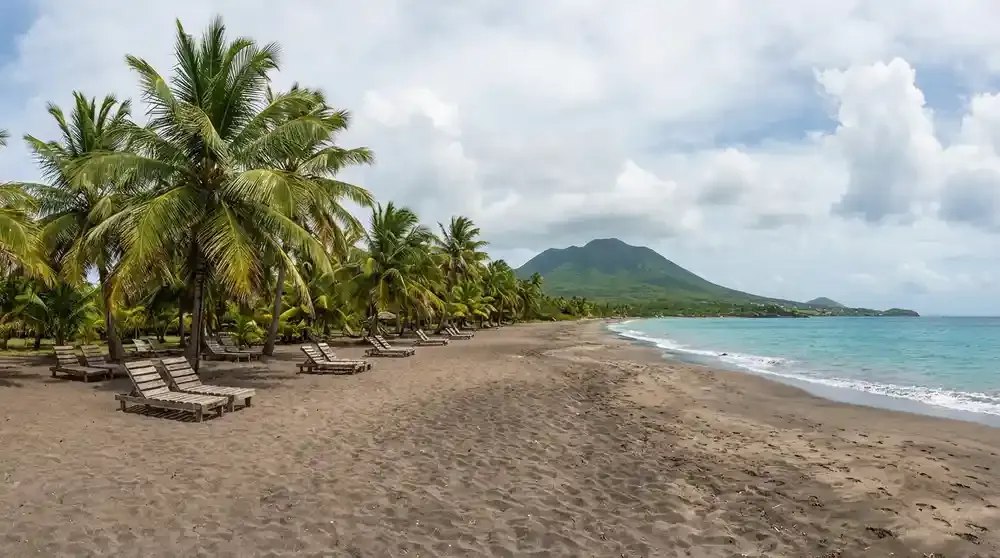 Pinney's Beach Nevis panoramic view with three miles of dark volcanic sand meeting turquoise Caribbean Sea, tall coconut palm trees providing shade, e